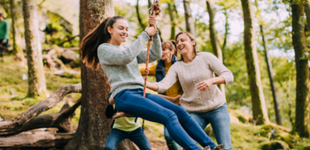Young person swinging on a swing that is hanging from a tree being pushed by friends and family.